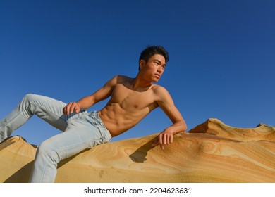 Bare-chested Young Man  Sit On A Large Stone On The Beach.