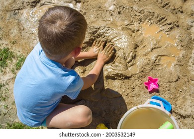 Barefeet Kid Playing With Wet Sand. Little Boy Kneads And Models Mud 
On Summer Sunny Day.