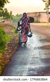 A bare-feet woman carrying water pots to fetch drinking water from a deepwell hand pump. This is a common practice or tradition as the scarcity of water in rural regions of India is a well known fact.