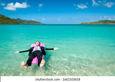 Barefoot Businessman Floating On A Bright Pink Pool Raft In Tropical Blue Waters