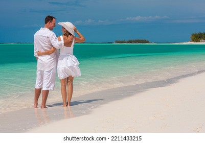 Barefoot Caucasian Couple In White Clothes Carefree Outdoors By The Turquoise Ocean On Tropical Luxury Caribbean Resort Island Under Blue Sky