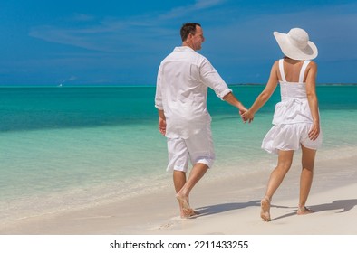 Barefoot Caucasian Couple In White Clothes Walking Carefree Outdoors By The Ocean On Tropical Luxury Caribbean Resort Island