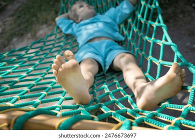 barefoot child relaxes while lying in a hammock. Lifestyle. enjoy life. Summer holidays. Happy childhood concept. Entertainment for children. Focus on feet
