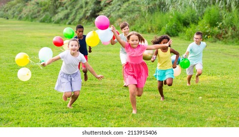 Barefoot children running through field with balloons in hands and smiling. - Shutterstock ID 2113915406