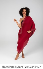 Barefoot confidence wrapped in ruby shimmer—she glows with effortless elegance, her scarlet shawl cascading like liquid starlight, turning the minimalist studio into a runway of radiant poise tonight