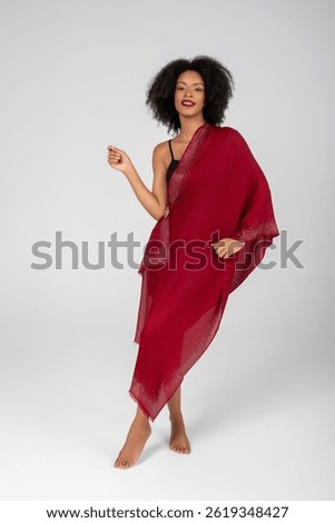 Barefoot confidence wrapped in ruby shimmer—she glows with effortless elegance, her scarlet shawl cascading like liquid starlight, turning the minimalist studio into a runway of radiant poise tonight