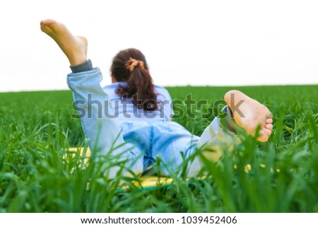 barefoot curly redhead woman lying in fresh green grass reading a book.A back picture of a woman lying on spring green grass. summer time season. unrecognizable person