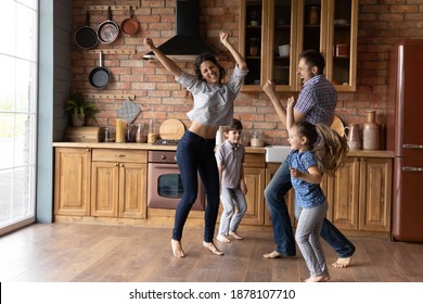 Barefoot Dances. Overjoyed Millennial Family With Little Daughter Son Having Fun Listening To Music Dancing. Active Mom Dad And Two Junior School Age Kids Jump At Kitchen Celebrate Moving To New Home