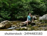 Barefoot, female teen kick water into the air as she sits on a rock in Horse Creek.  Horese Creek is in the Cherokee National Forest in Tennessee.