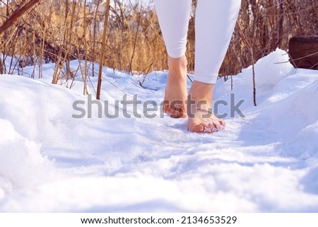 Barefoot girl in the snow. Walking in the snow in winter. Hardening. Cryotherapy. Healthy lifestyle. Legs of a girl on a path in winter.