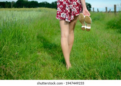 Barefoot girl walking on green grass. Slim girl holding her shoes in hand, wearing colorful skirt. Summer in Poland, beautiful farmland in Lower Silesia.