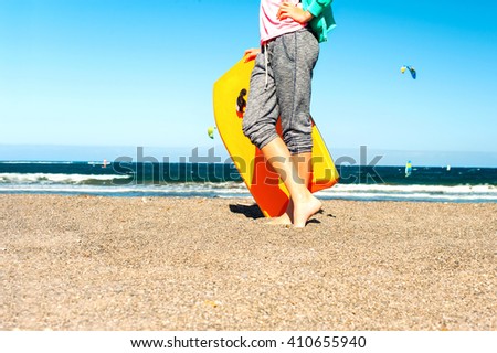 Barefoot legs and feet of young girl standing and holding surfboard on Atlantic ocean sandy coast. Canary islands, Tenerife, Spain. Multicolored vibrant outdoors horizontal image.