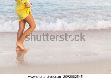 Barefoot legs of a girl in yellow dress walking on a wet sandy beach