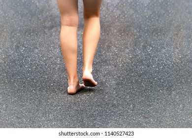 Barefoot Legs Of A Young Girl Walking On A Dirty Road.