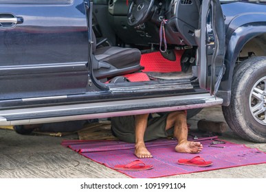 A Barefoot Man Working Under A Car.