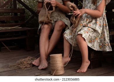 Barefoot Mother And Daughter Crocheting From Jute In Rustic Terrace At Summer Time