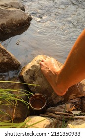 Barefoot Next To Riverside Water, Rocks And Raw Cacao Cup