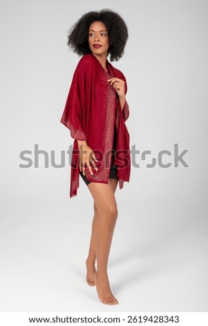 Barefoot poise wrapped in ruby shimmer; she gazes beyond with quiet resolve, a jeweled shawl floating around graceful limbs, turning minimal studio light into whispers of evening elegance tonight....
