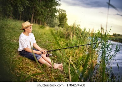 Barefoot Teen Boy Holding Fishing Rod And Looking In River, Waiting For A Catch