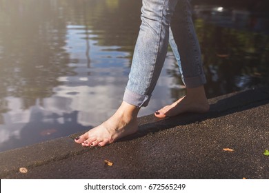 Barefoot Woman In Blue Jeans Walking On A Water Edge