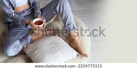 Barefoot woman with cup of tea relaxing on pouf at home. Banner for design