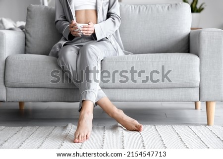 Barefoot woman with cup of tea sitting on sofa at home