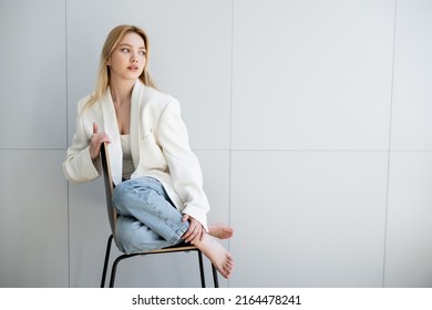 Barefoot Woman In Jeans And Jacket Sitting On Chair At Home