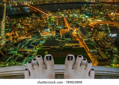 Barefoot woman on top of a building thinking of suicide, over Osaka City Central business district at night in Japan. Depression and stress urban life concept.
