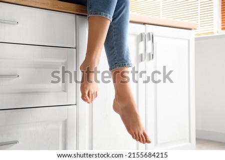 Barefoot woman sitting on counter in kitchen