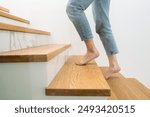 Barefoot woman standing on a wooden staircase at home. Cropped shot of female walking upstairs in apartment. Person climbing on stairs in building