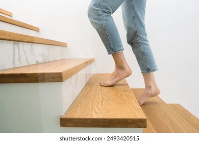 Barefoot woman standing on a wooden staircase at home. Cropped shot of female walking upstairs in apartment. Person climbing on stairs in building