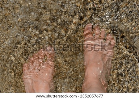 Barefoot women's feet close-up in clear water on the sandy bottom. The glare of the sun on the water.
