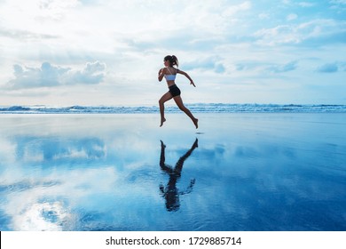 Barefoot young girl with slim body running along sea surf by water pool to keep fit and burning fat. Beach background with blue sky. Woman fitness, jogging sports activity on summer family vacation. - Shutterstock ID 1729885714