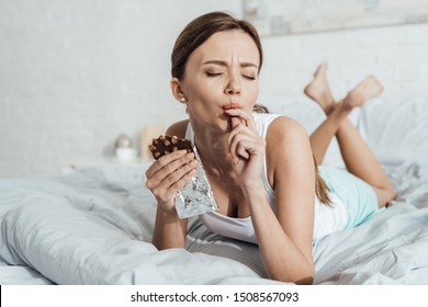 Barefoot Young Woman Eating Chocolate With Nuts In Bed