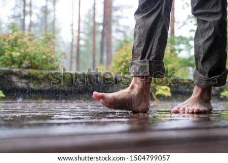 Barefooted female legs in the pouring summer rain, on a blurred background. Close-up.