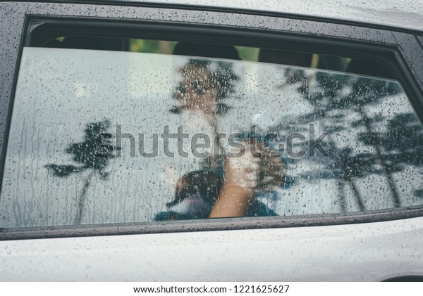 Barely visible romantic outlines\
of a bride girl, seen through raindrops on the gray car\
window