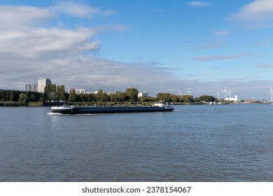 A barge going down the Scheldt River in Antwerp, Belgium, with wind turbines in the background and water in the foreground.