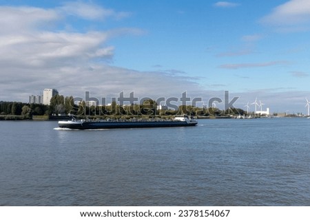 A barge going down the Scheldt River in Antwerp, Belgium, with wind turbines in the background and water in the foreground.
