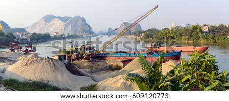 Barge loading sand by the crane. River in mountain region in Vietnam