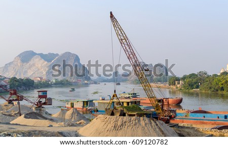 Barge loading sand by the crane. River in mountain region in Vietnam