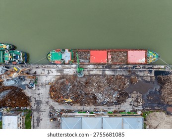 A barge is unloading debris at a dock while workers manage materials near the edge of the river. Boats are tied up at the dock, and the area is busy with activity.