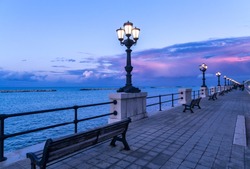 Bari Seafront At Sunset Purple And Blue Sky Landscape Panorama. Bench And Street Lamp Near The Sea
