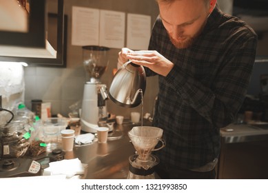 Barista at bar counter is making pourover coffee at the coffee shop. Male barista is concentrated on preparing pourover coffee at the cafe.