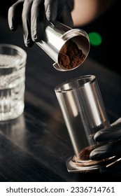 barista in black latex gloves pouring ground coffee in aero press, alternative brewing method - Shutterstock ID 2336714761