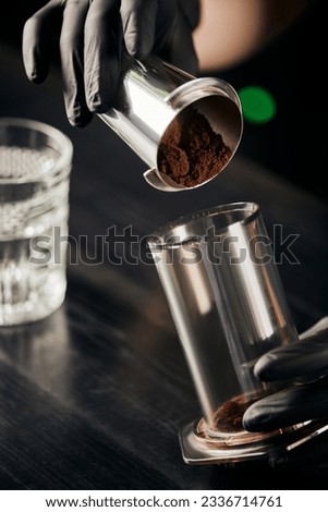 barista in black latex gloves pouring ground coffee in aero press, alternative brewing method