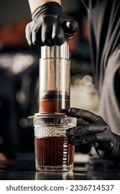 barista in black latex gloves pressing ground coffee in aero press, alternative brewing method - Shutterstock ID 2336714537