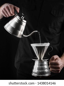 A barista brews coffee by an alternative method in pour over, coffee filter, glass teapot on a wooden tray on a dark background. - Shutterstock ID 1438014146