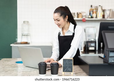 Barista Cafe Or Bartender Working At Coffee Shop. Asian Barista Woman Using Laptop Computer In Coffee Shop With Happy And Smile. Small Business And Purchase Concept