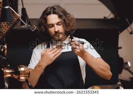 Barista control grounds roasting process of beans, test aroma. Man working at coffee production.