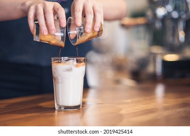 Barista is filling milk with espresso to prepare ice latte, cloesup detail view with copyspace.